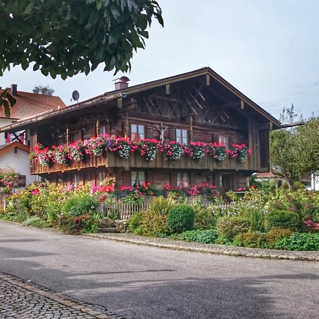 Ein großes Holzhaus mit Balkon voller Blumen und blühendem Garten am Starnberger See