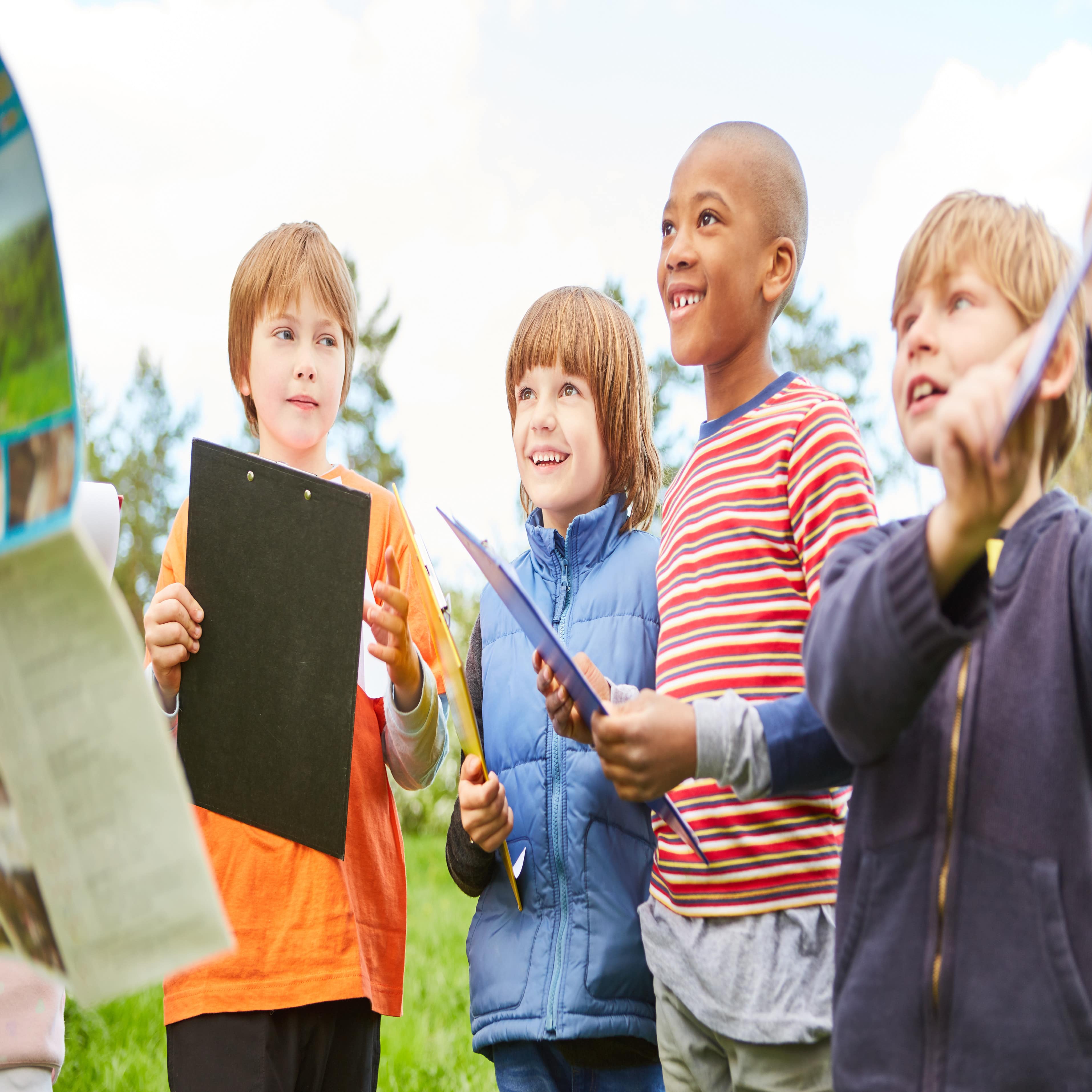 4 Kinder mit Klemmbrettern in der Hand lauschen Anweisungen bei einer Schnitzeljagd.