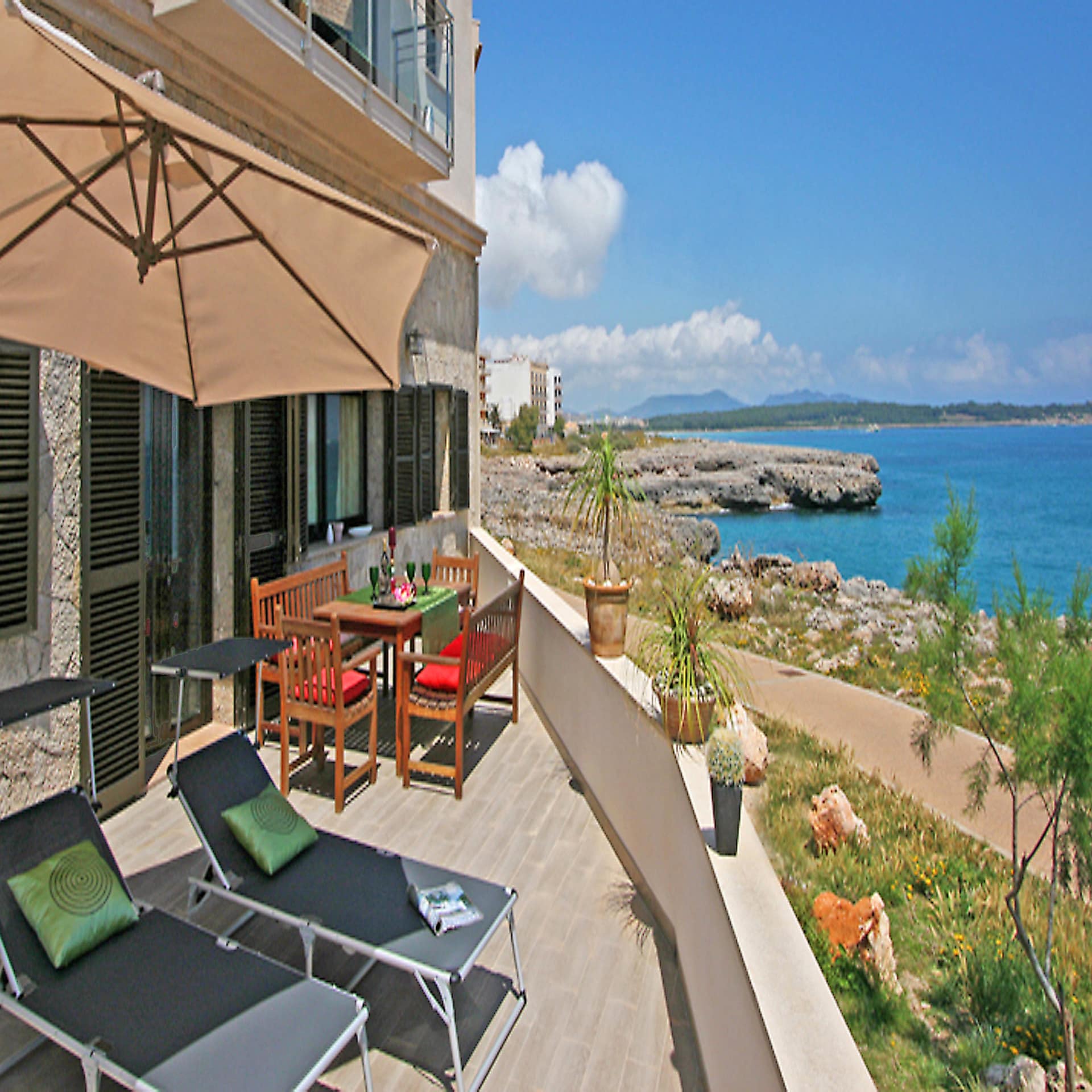 Terrasse mit Sonnenliegen, Schirm und Sitzgelegenheiten sowie Blick auf das Meer. 