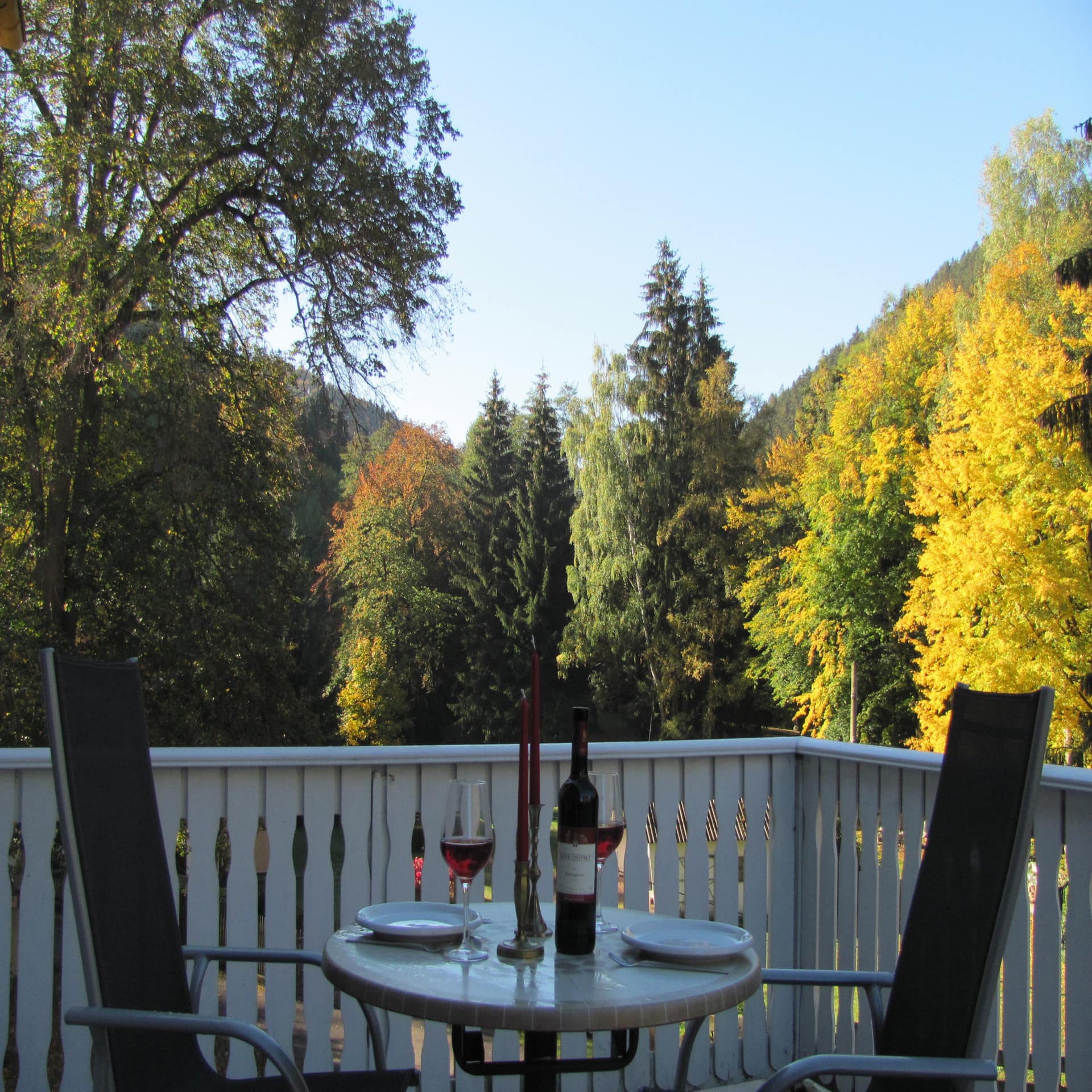 Balkon mit Tisch, 2 Stühlen, Wein und Kerzen sowie Blick auf Bäume. 