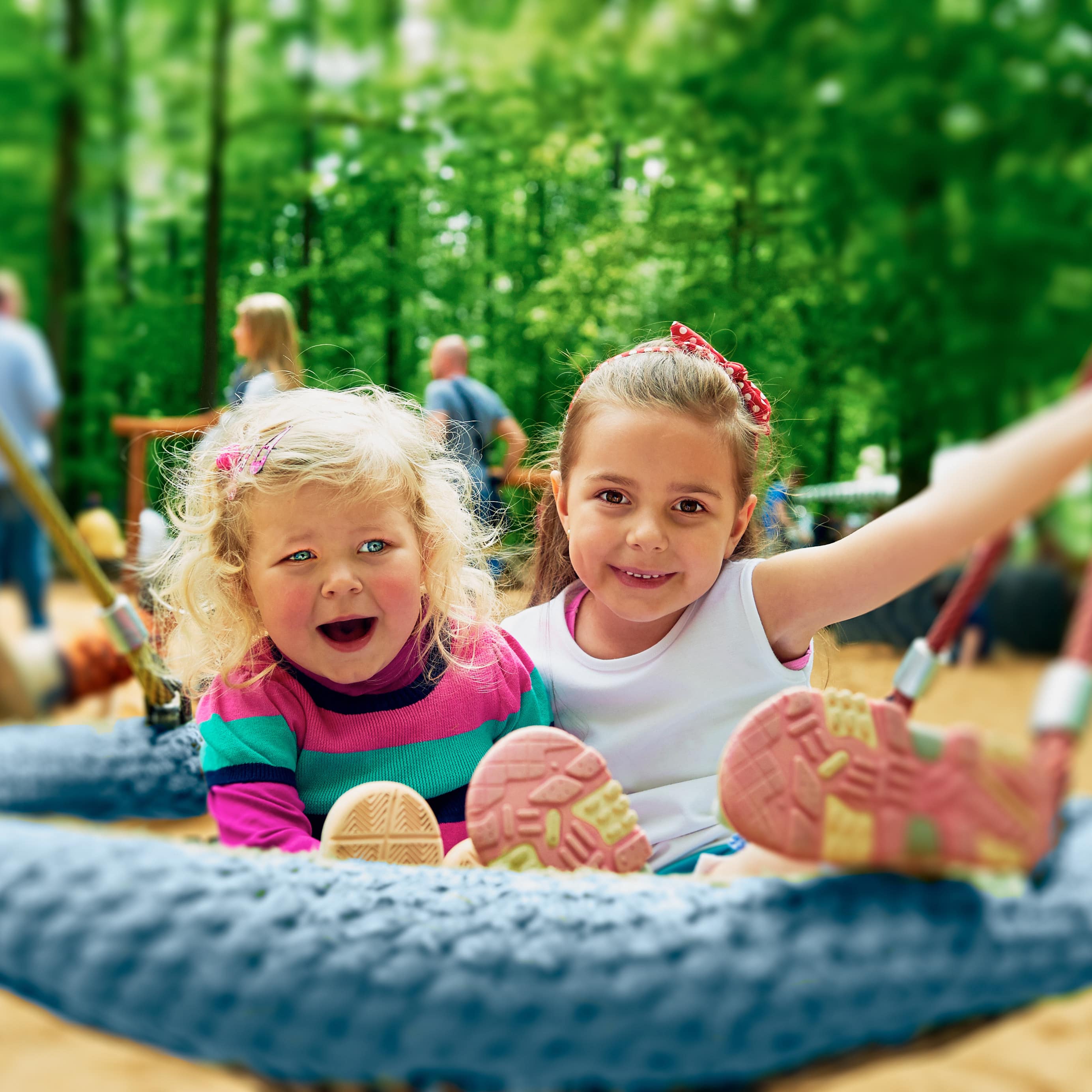 2 Mädchen auf einer Schaukel auf einem Waldspielplatz.