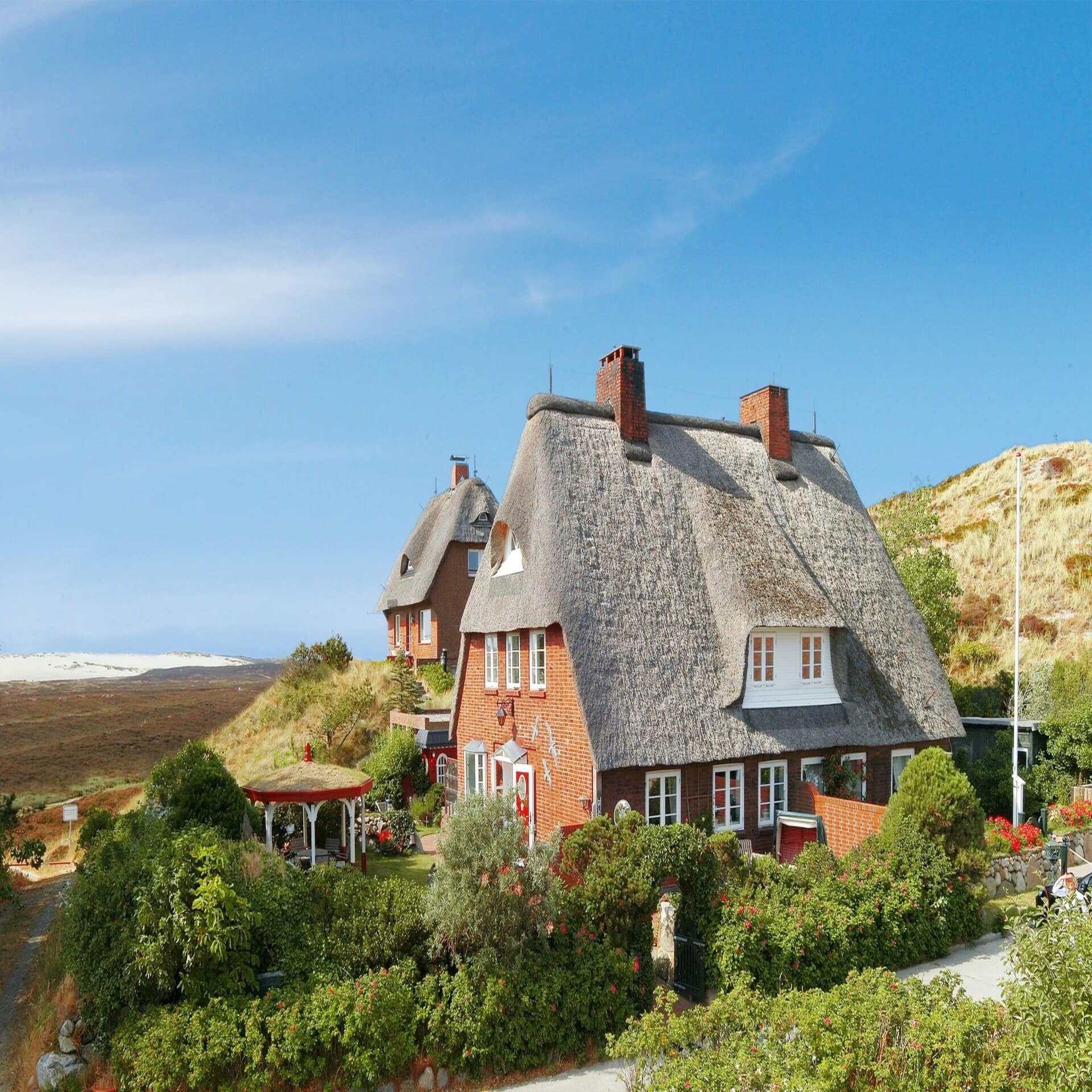 2 rote Häuser mit Reetdach und Garten in der Nordseelandschaft.