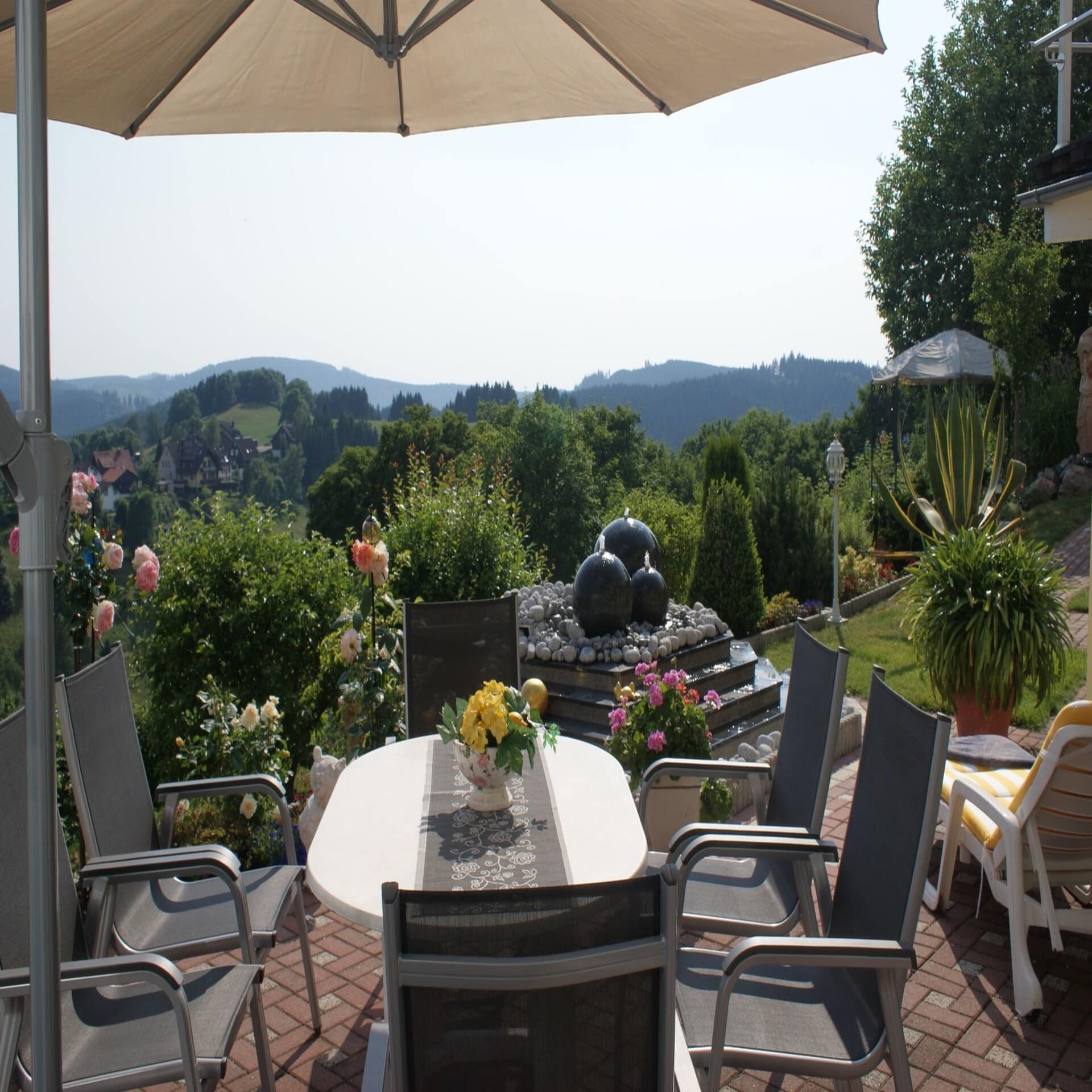 Terrasse mit Tisch, Sonnenschirm und Stühlen sowie Panoramablick auf die ländliche Umgebung.