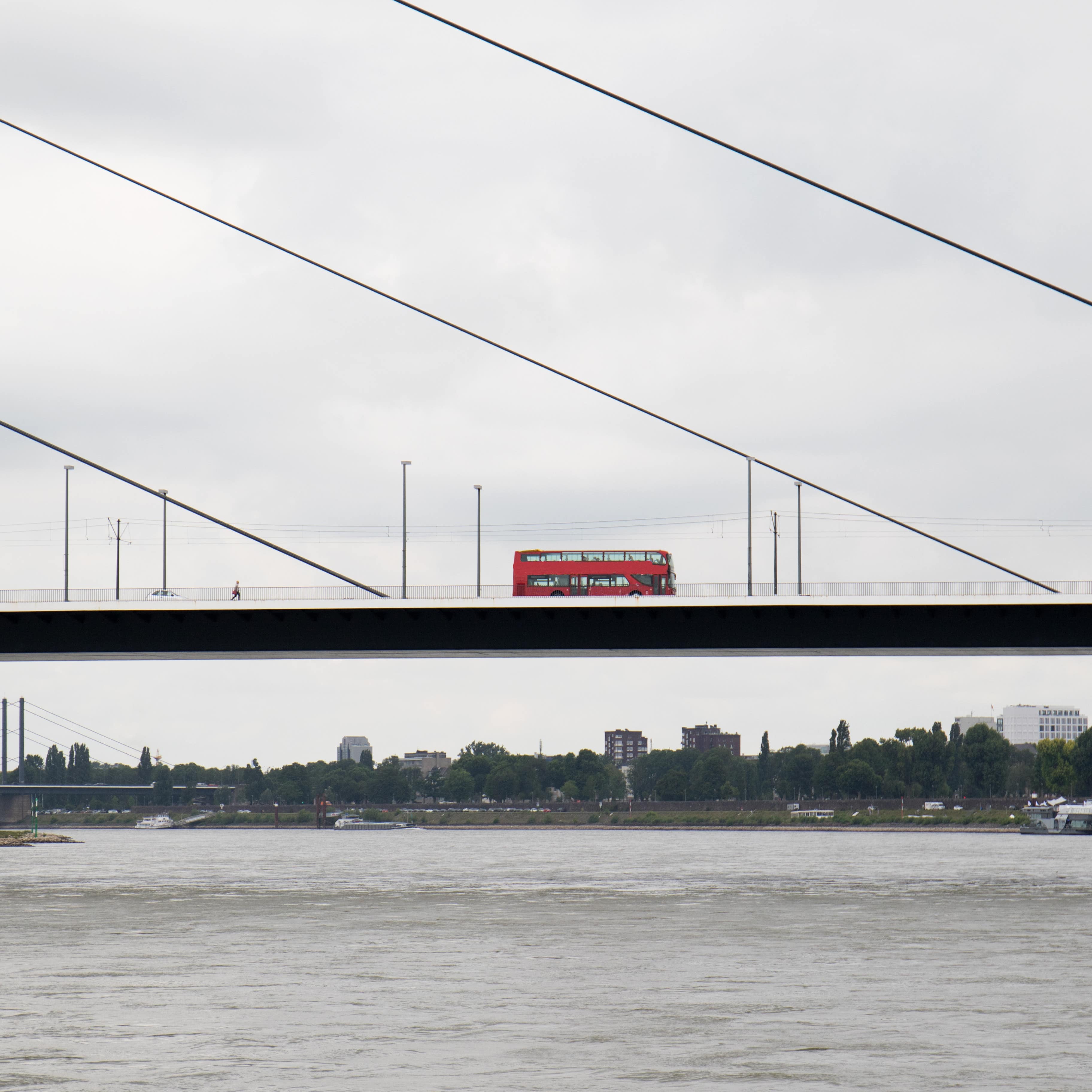 Blick aus der Entfernung: Ein roter Doppeldeckerbus fährt auf einer Brücke über den Rhein.