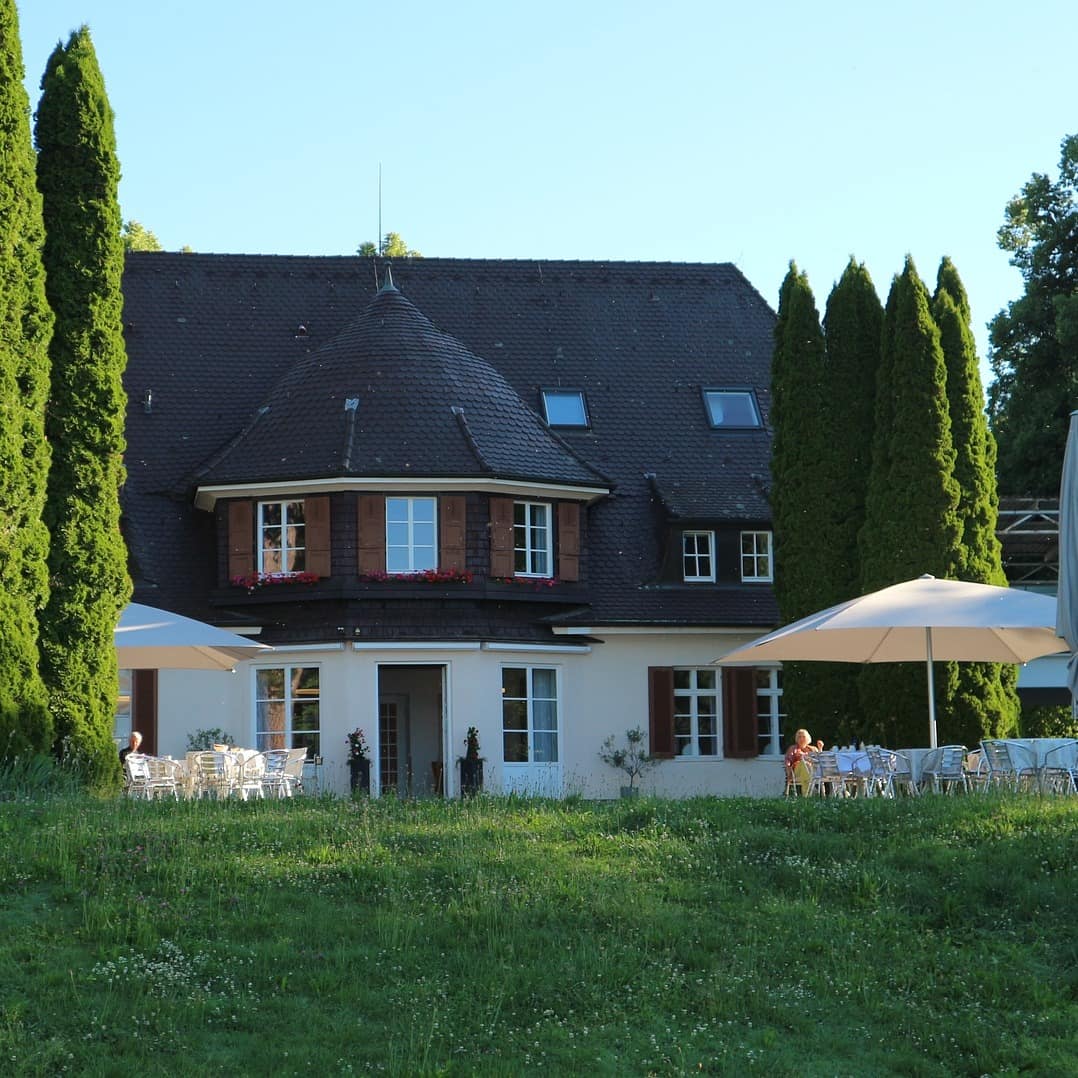 Blick auf ein Haus in Friedrichshafen mit Stühlen und Sonnenschirmen inmitten der Natur