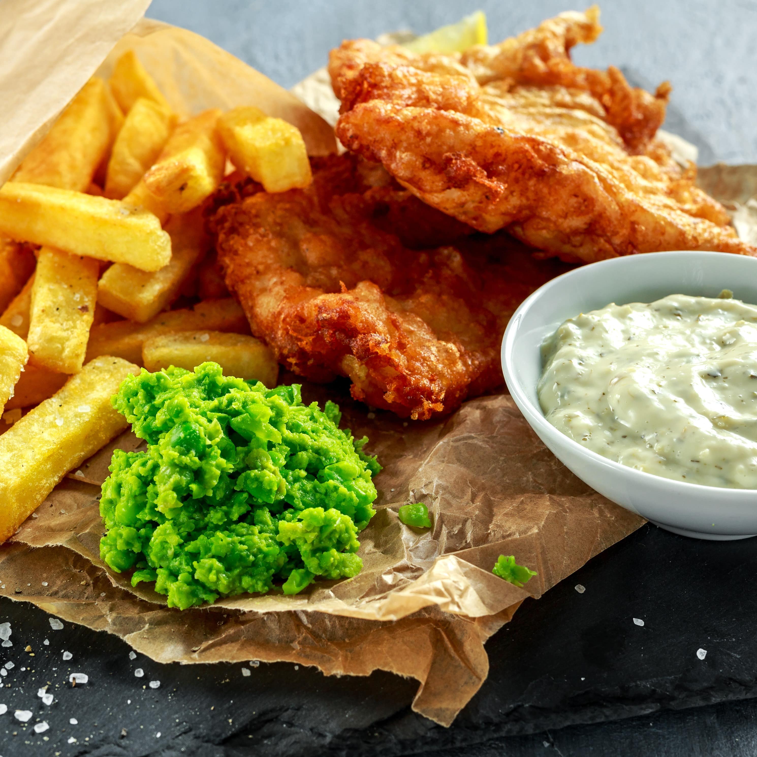 Auf einer Schieferplatte werden Fish & Chips mit Erbsenpüree serviert.