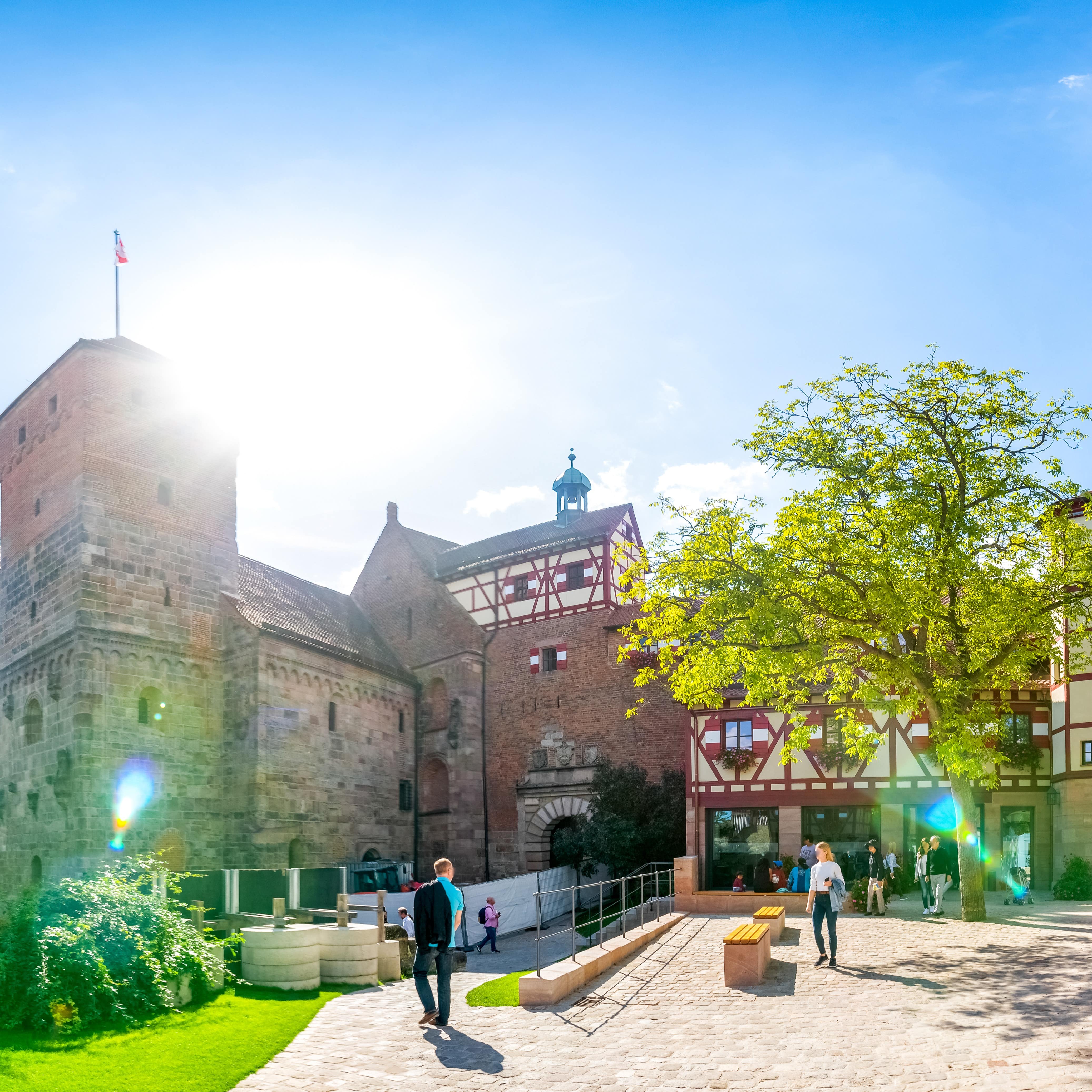 Blick auf die Kaiserburg und gelb-rote Fachwerkhäuser. Davor Erwachsene und Kinder.