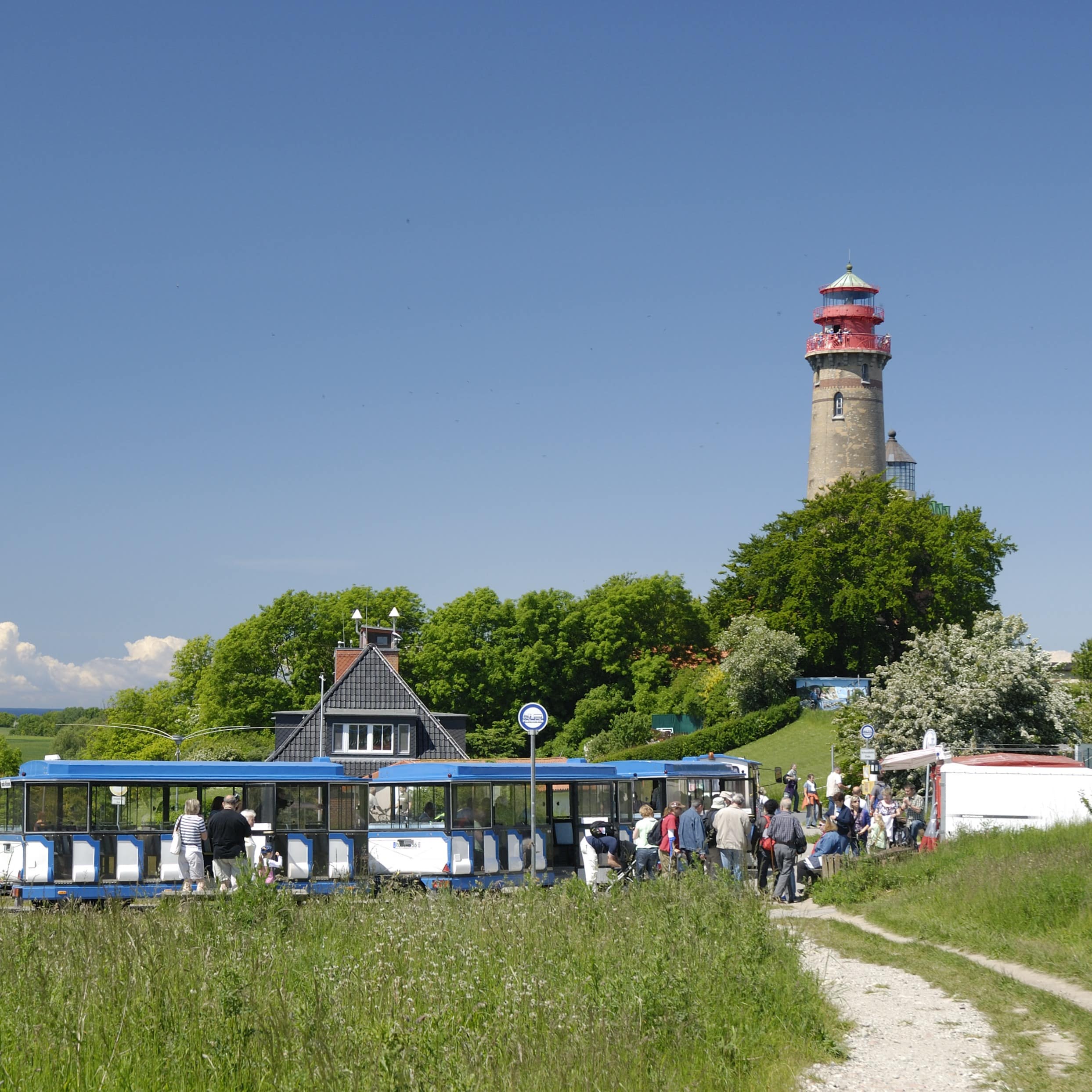 Blau-weiße Besucherbahn am Kap Arkona, im Hintergrund der Leuchtturm. Passagiere steigen ein und aus.