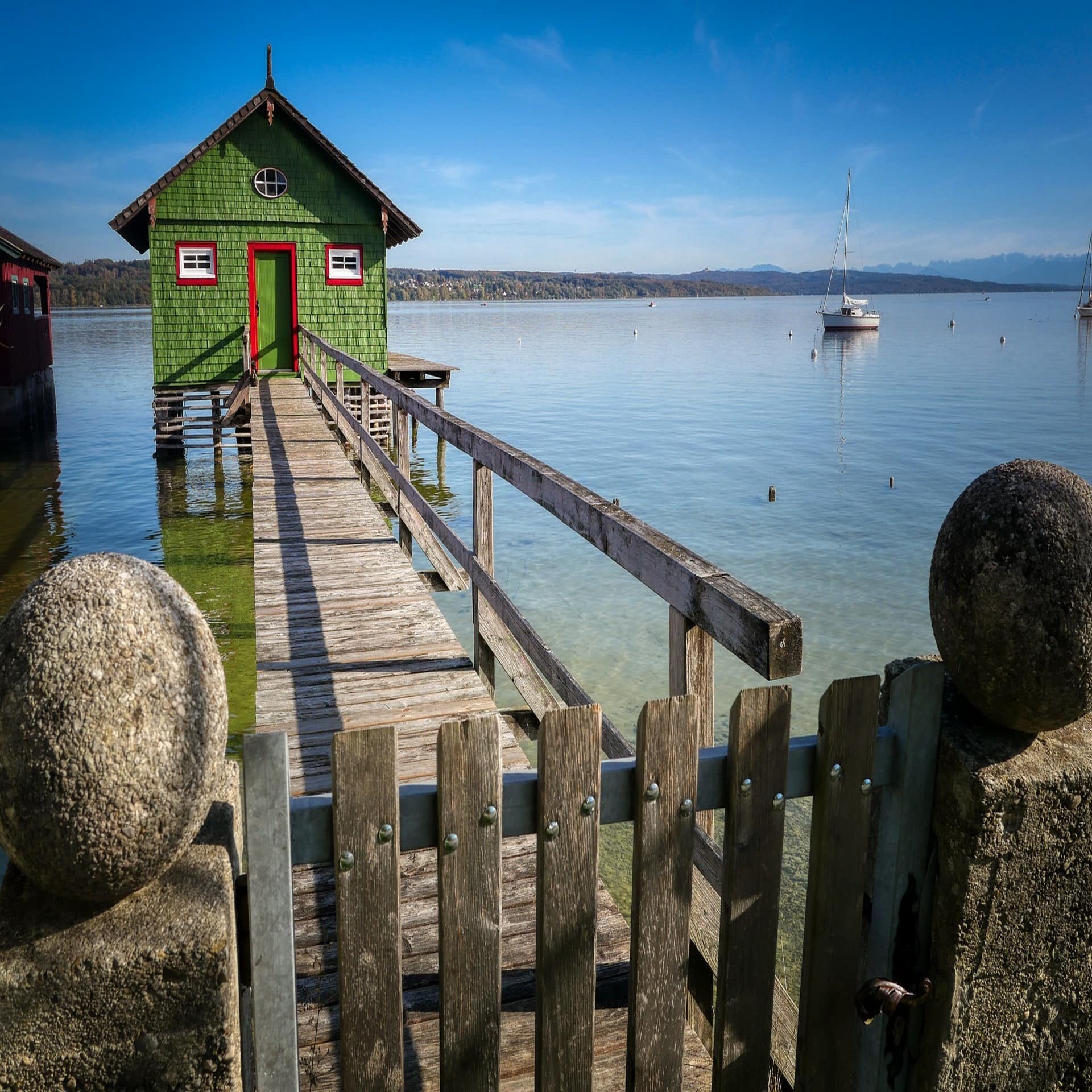 Blick einen Steg entlang auf ein grünes Bootshaus. Rechts ist ein Segelboot zu sehen.