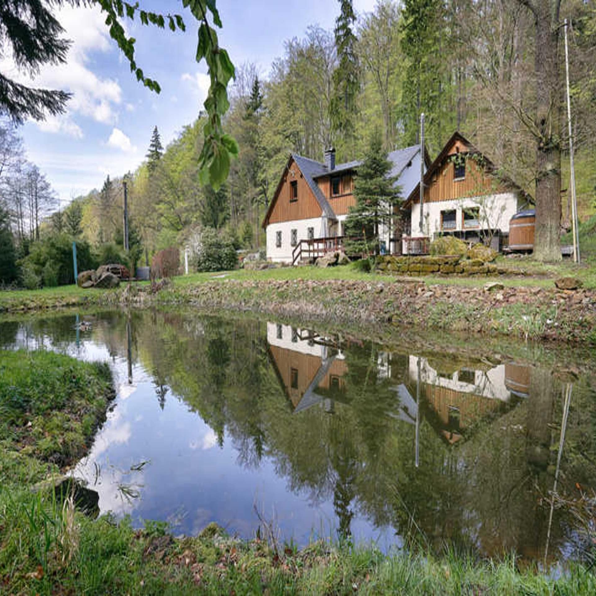 Haus in Alleinlage im Wald, davor ein kleiner See in dem sich das Haus spiegelt.