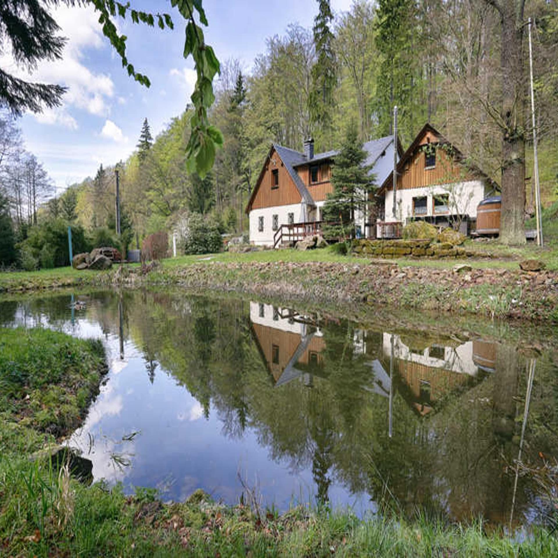 Haus in Alleinlage im Wald, davor ein kleiner See in dem sich das Haus spiegelt. 