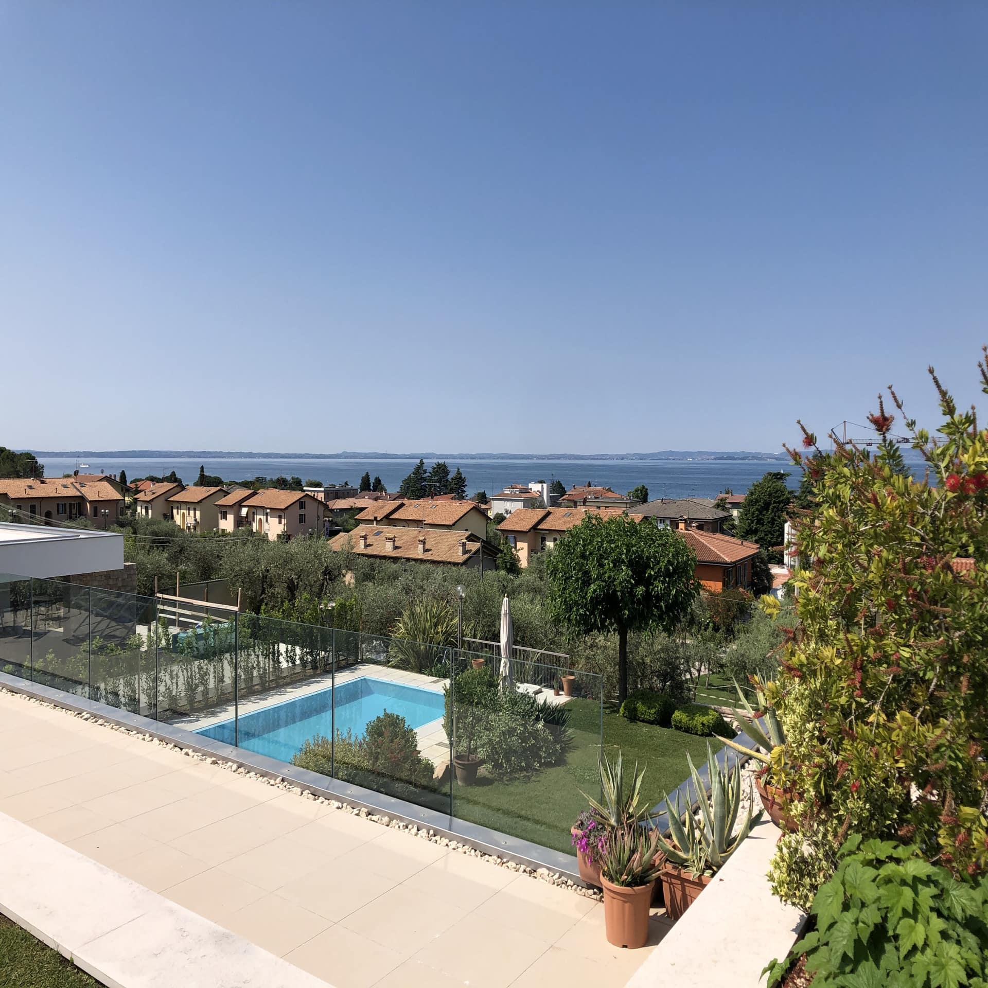 Blick von einer Terrasse auf einen Garten mit Pool, Häuser von Bardolino und den Gardasee. 