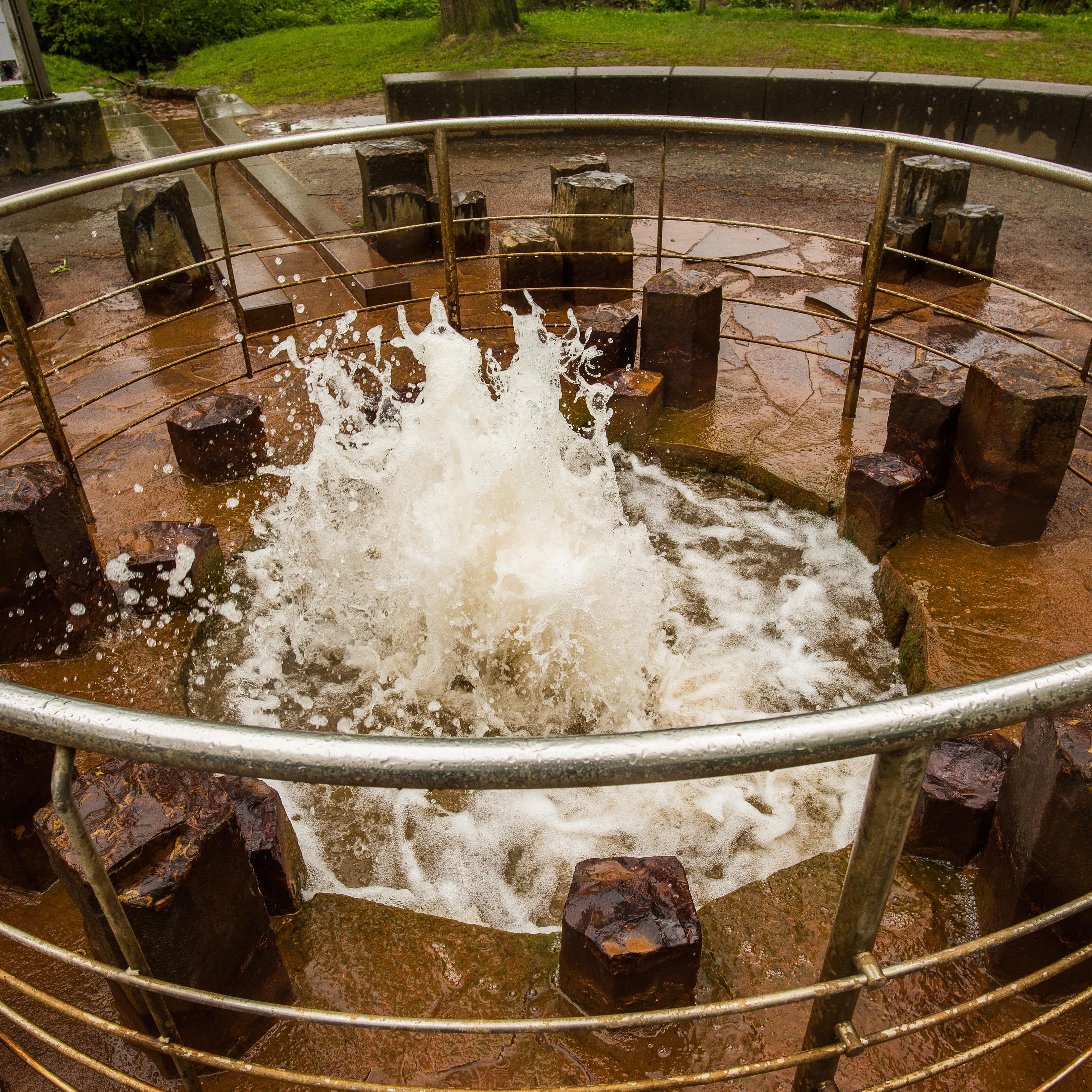 Aus dem Kaltwasser-Geysir sprudelt Wasser. Ringsherum eine Metallabsperrung.