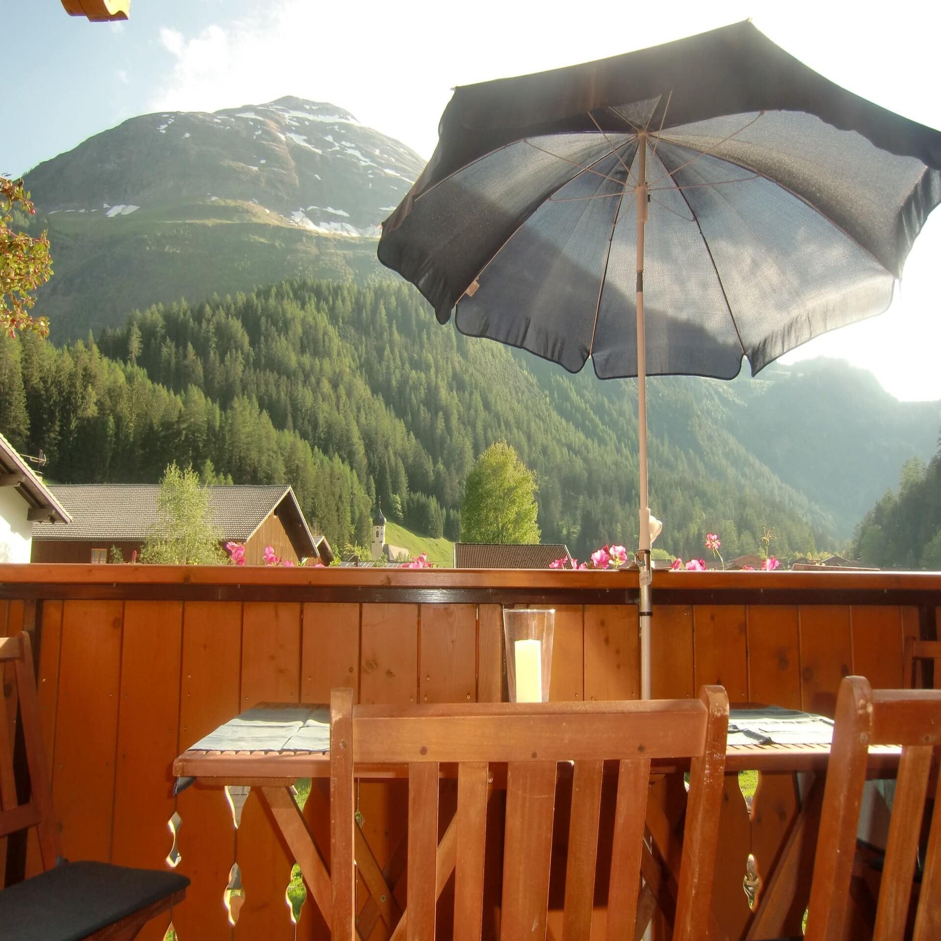 Blick vom Holzbalkon mit Sonnenschirm auf die sommerlichen Berge.