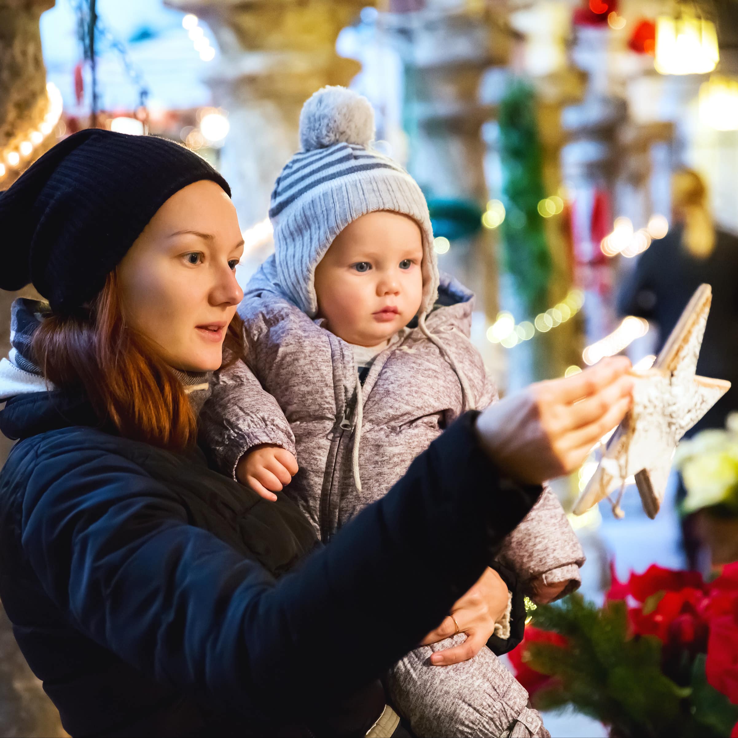 Mutter und Baby schauen einen Holzstern auf dem Weihnachtsmarkt an.