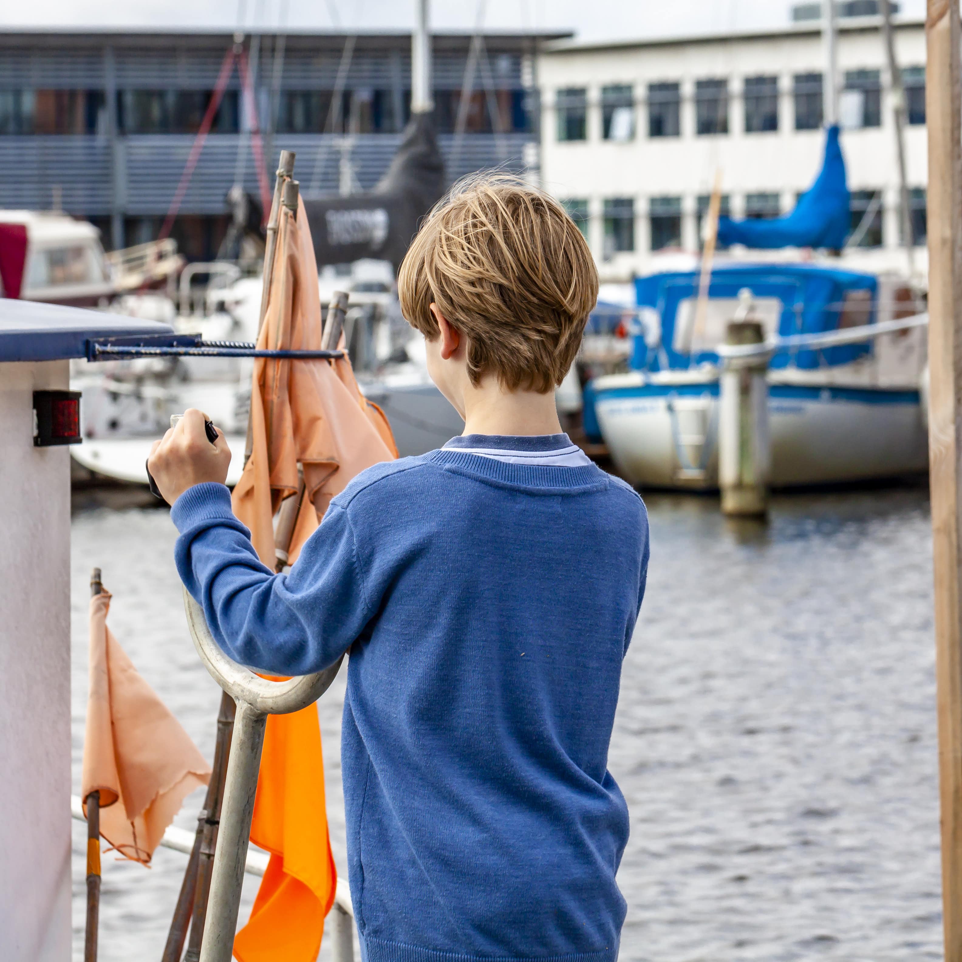 Ein Junge in blauem Pulli auf einem Boot im Hafen.