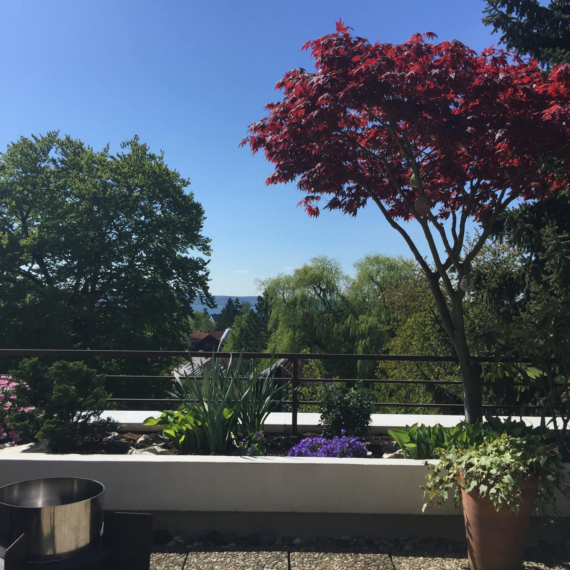 Balkon mit Blumen einer Ferienwohnung am Ammersee mit Seeblick, zwischen Bäumen ist der See zu sehen