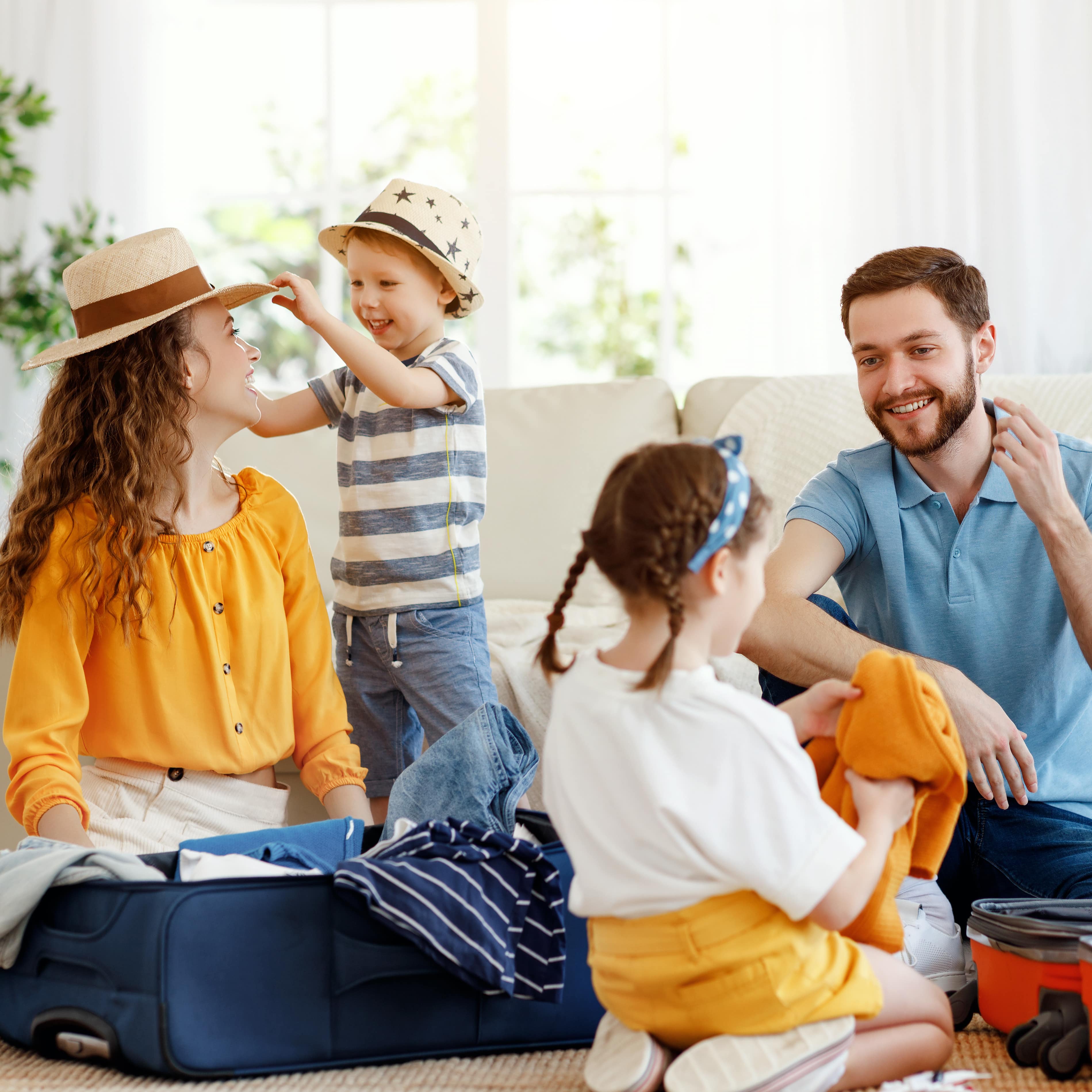 4-köpfige Familie mit 2 geöffneten Koffern in einem hell eingerichteten Wohnzimmer. Image URL: